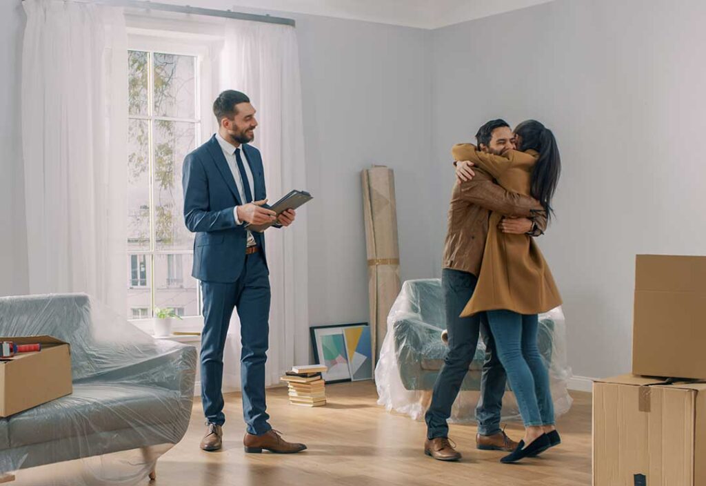 A family and real estate agent reviewing documents at a kitchen table scattered with papers and a laptop.