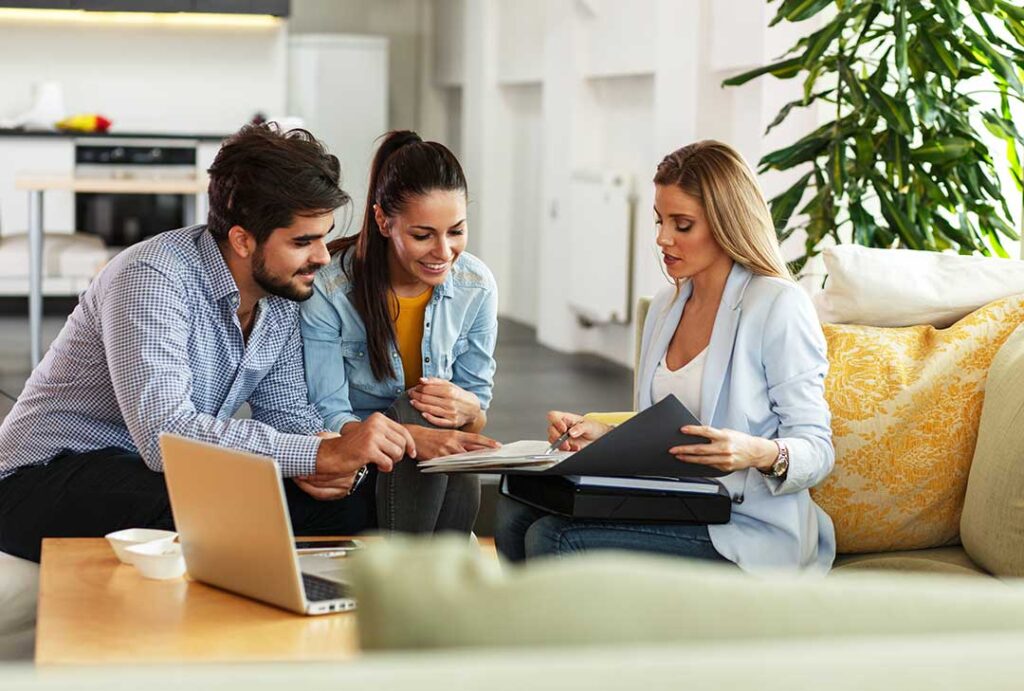 A couple reviews a printed home listing beside a laptop and property photographs.